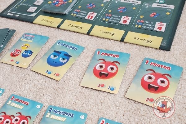 A picture of the game subatomic from Genius Games featuring cute faced atomic particle characters on cards.