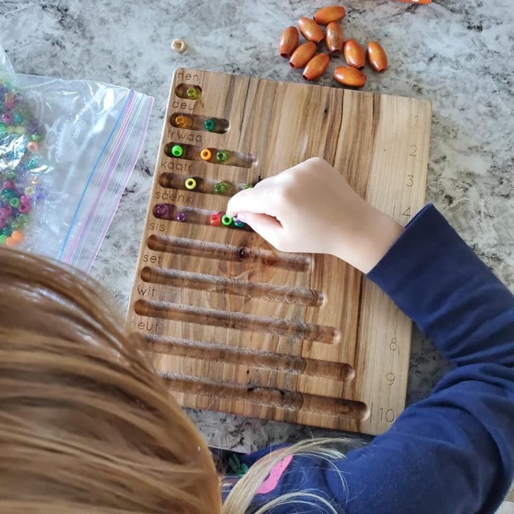 Little girl adding beads to a wooden counting board with Michif words